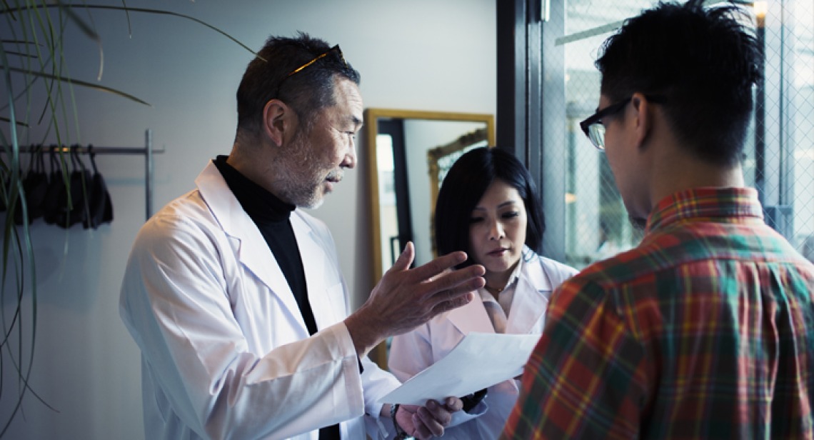 doctor giving notes to intern in front of patient